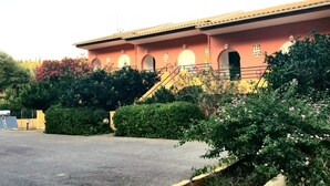 A building with a yellow facade, multiple arched windows, and a staircase leading to the entrance. - Corfu Escape Three (Corfu)
