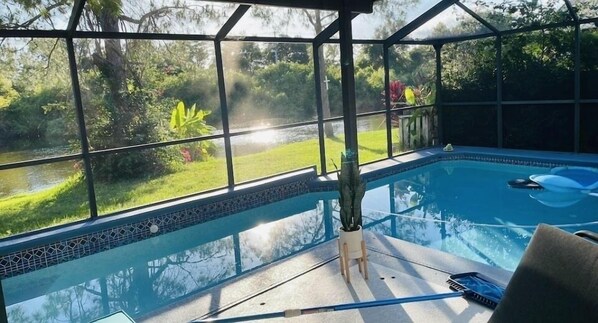 A glass-enclosed swimming pool with a view of a garden and a body of water outside. - Pool, pool table, 4 bedroom, 2.5 bath home with very high rating! (Brandon)
