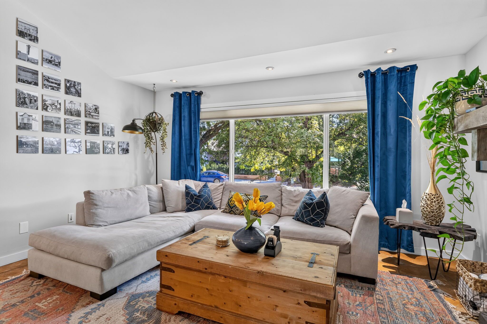 Ein modernes Wohnzimmer mit einem Ecksofa, einem Holztisch und einem großen Fenster mit blauen Vorhängen.