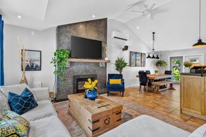 Een moderne woonkamer met een open haard, een flatscreen televisie en een eethoek met een houten tafel en stoelen.