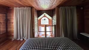 A room with wooden walls and ceiling, a checkered bedspread, and a window with a wooden frame and curtains. - Cozy little cabin with creek access.  Great for fishing or tubing! (Landisburg)