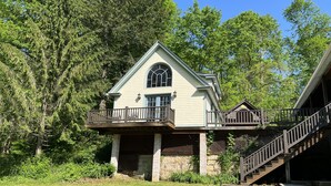 A two-story house with a balcony, a stone foundation, and a wooden staircase leading to the entrance. - Cozy little cabin with creek access.  Great for fishing or tubing! (Landisburg)