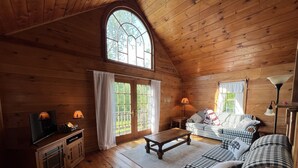 A cozy log cabin interior with a wooden floor, a television, a sofa, and two lamps. - Cozy little cabin with creek access.  Great for fishing or tubing! (Landisburg)