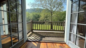 A wooden deck with a railing, a glass door, and a view of a green landscape with trees. - Cozy little cabin with creek access.  Great for fishing or tubing! (Landisburg)
