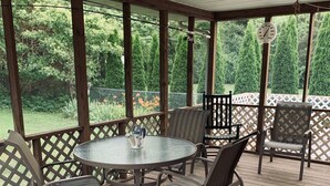 Une terrasse couverte avec une table ronde et des chaises, entourée d’une plateforme en bois et d’une clôture blanche en treillis.