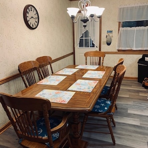A dining room with a wooden table, six chairs, and a wall clock.