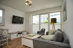 Un salon moderne avec un canapé, des fauteuils, une table basse, un téléviseur et une lampe.