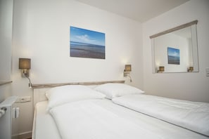 Un lit bien fait, avec du linge de lit blanc, une tête de lit en bois et deux lampes fixées au mur.