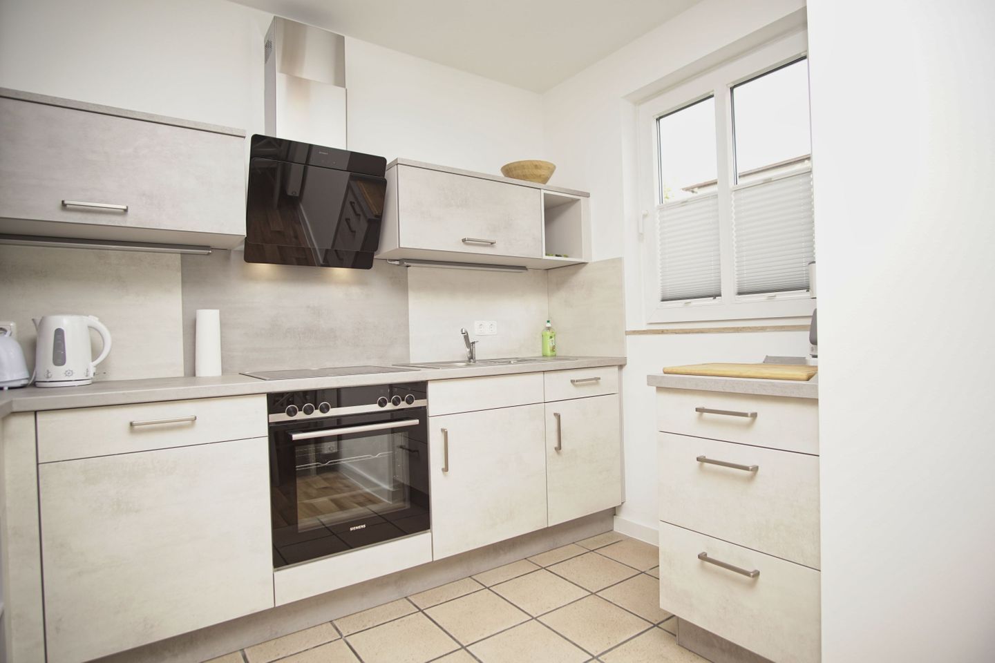 Una cocina compacta con horno integrado, hervidor y tabla de cortar sobre la encimera.