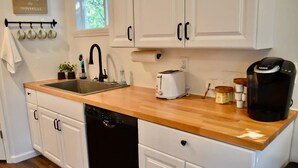 A kitchen with white cabinets, a wooden countertop, a Bosch dishwasher, a toaster, and a coffee maker. - Cute tiny home with everything you need! (Cedar Falls)