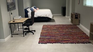 A bedroom with a bed, desk, chair, and a colorful rug. - Studio Basement Central El Paso (El Paso)