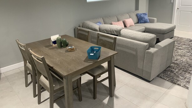 A dining area with a wooden table and chairs, a gray sofa, and a gray rug. - Studio Basement Central El Paso (El Paso)