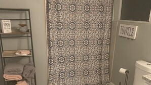A bathroom with a shower curtain, a toilet, a shelf with towels, and a sign indicating the towel area. - Studio Basement Central El Paso (El Paso)