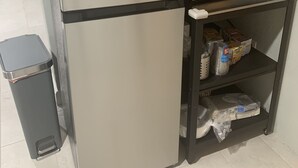 A compact kitchen with a stainless steel refrigerator, a microwave, and a small shelf with packaged goods. - Studio Basement Central El Paso (El Paso)