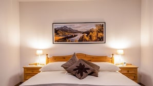 Un lit bien fait, avec une tête de lit en bois, deux tables de chevet avec des lampes et, au-dessus du lit, un tableau représentant un paysage.
