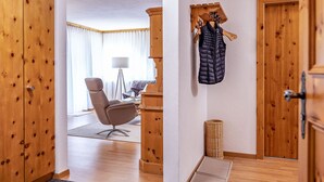 Une chambre d’hôtel avec un plancher en bois, une moquette grise, un bureau avec une chaise, une lampe et un porte-manteau avec une veste.