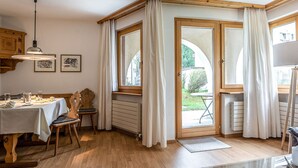 Un coin repas avec une table dressée pour deux personnes, des chaises en bois, un radiateur et une vue sur l’extérieur grâce à une porte vitrée.