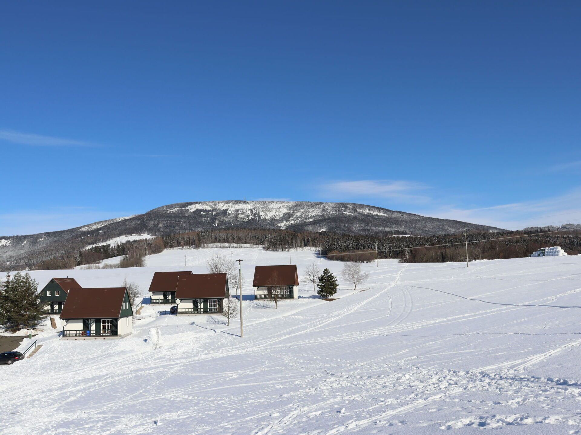 Schneebedeckte Landschaft mit einem Berg im Hintergrund und einem Gebäude mit braunem Dach im Vordergrund.