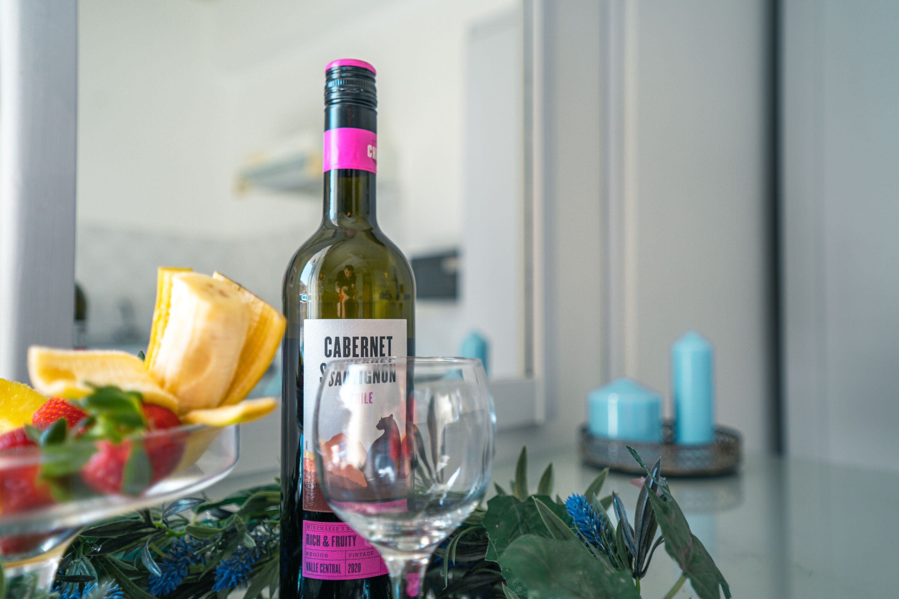 A bottle of Cabernet Sauvignon wine, a glass, and a bowl of fruit on a table.