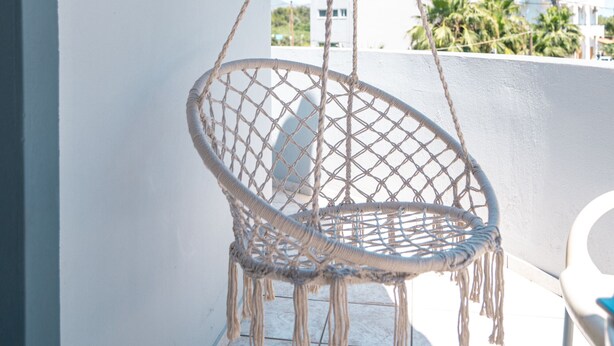 A macrame hanging chair on a balcony with a view of palm trees and buildings. - Rodi blue (Malevizi)