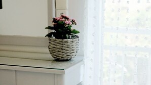A white table with a wicker basket containing pink flowers, a white candle, and a blue cushion. - Rodi blue (Malevizi)