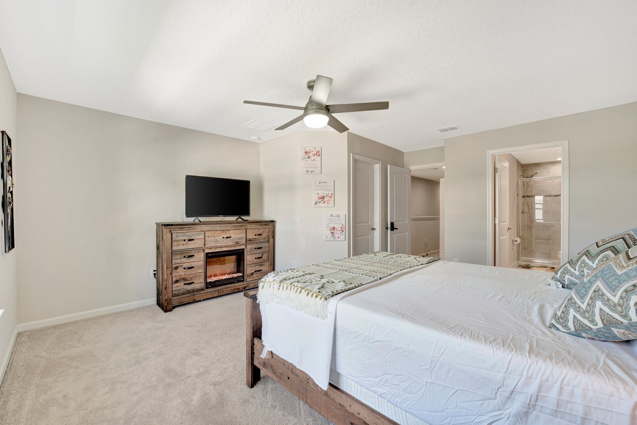 A bedroom with a bed, a wooden dresser, a ceiling fan, and a TV.