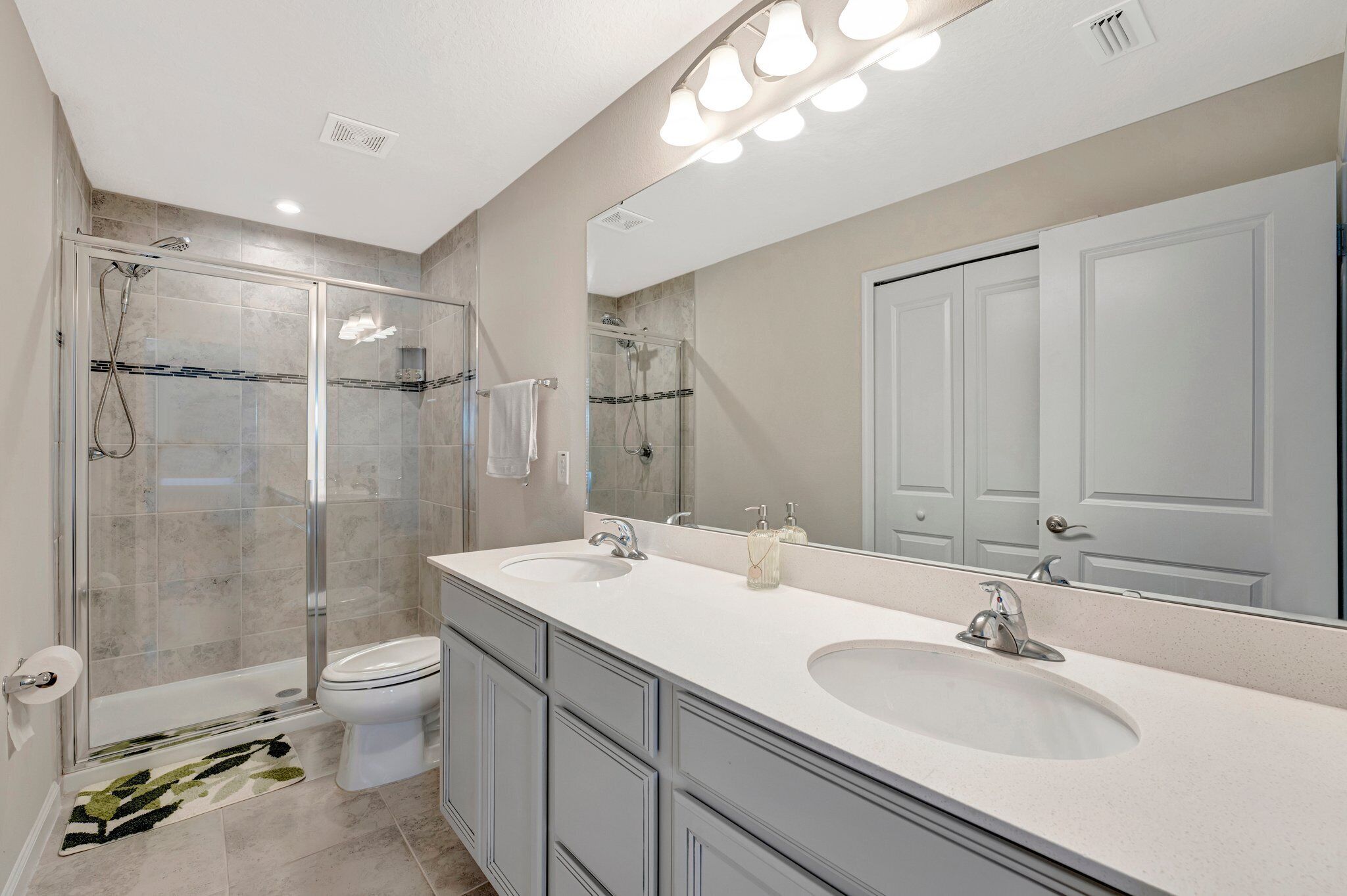 A modern bathroom with a glass-enclosed shower, a double sink vanity, and a large mirror.