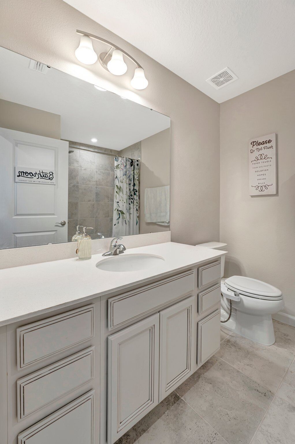 A bathroom with a white vanity, a large mirror, a shower with a floral curtain, and a toilet.