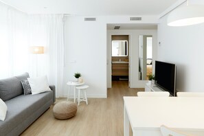 A modern living room with a grey sofa, a small round table with a plant, a white TV stand, and a wooden floor. - Beautiful loft in Santiago Bernabéu, Madrid (Madrid)