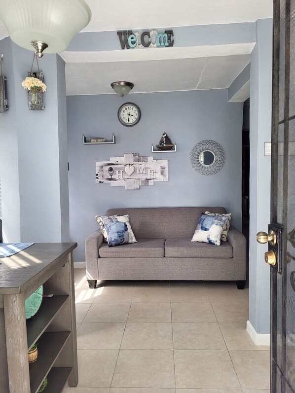 A living room with a grey sofa, a wooden table, and a wall-mounted clock.