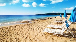 A beach with white lounge chairs and blue umbrellas, sandy beach, and calm sea.
