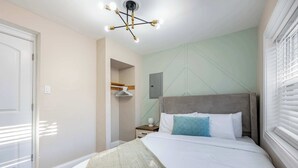 Un dormitorio con cama, mesita de noche, lámpara colgante y ventana con persianas.