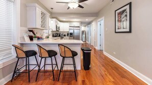 Una cocina moderna con armarios blancos, una isla central con taburetes y electrodomésticos de acero inoxidable, además de un ventilador de techo.