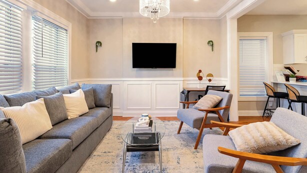 Un salón con un sofá gris, una mesa de centro y un televisor montado en la pared.