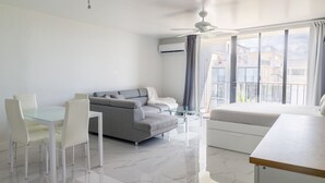 Un salon moderne avec une table à manger en verre, des chaises blanches, un canapé gris, un canapé blanc et un ventilateur de plafond.
