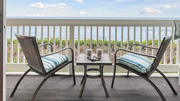 A balcony with two wicker chairs and a small table, overlooking a body of water. - Peaceful Beachfront Oasis-- Walk onto the sand! (Melbourne Beach)