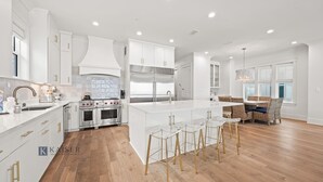 A modern kitchen with white cabinetry, stainless steel appliances, and a central island with bar stools. - Ocean Edge 9 | Beach Front, Plunge Pool, Boardwalk | Paradise Found by Kaiser (Orange Beach)