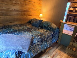 Una habitación de madera con una cama, una mesita de noche y una ventana.