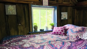 A cozy bedroom with a bed, a window with plants, and a sign on the wall. - Cozy Cabin: Peaceful Haven in the Heart of Nature (Green Mountain)