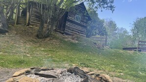 A rustic cabin surrounded by trees, a fire pit with rocks, and a grassy area. - Cozy Cabin: Peaceful Haven in the Heart of Nature (Green Mountain)