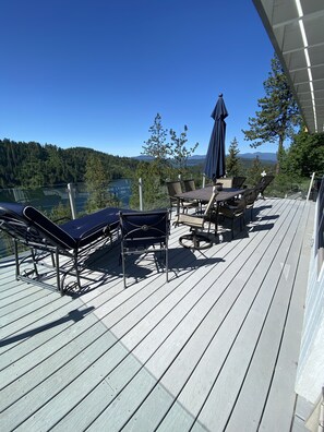 Une terrasse dotée de chaises longues et d’une table, offrant une vue sur un lac et des collines boisées.