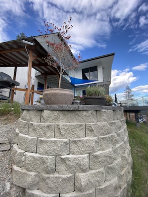 Une maison moderne dotée d’un mur de soutènement en pierre, d’un patio couvert et offrant une vue sur le ciel.