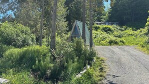 A gravel road curving through a forested area with a metal gate and a building in the background. - A-frame Shelter (T16) Oceanview Olympic Peninsula (Port Angeles)
