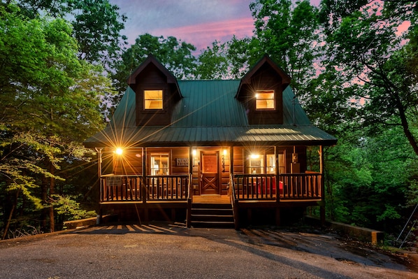 A two-story wooden cabin with a porch, a welcome sign, and a 'Carry On' sign.
