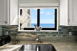 A kitchen with a view of the ocean through a window, a sink, and a decorative fish sculpture. - Superb oceanfront condo w/pool, sundeck, private balcony near pier for fishing, walking, crabbing (North Myrtle Beach)