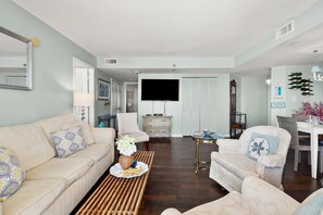 Un salon comprenant un canapé, des fauteuils, une table basse avec des collations, un téléviseur et un coin repas avec une table et des chaises.