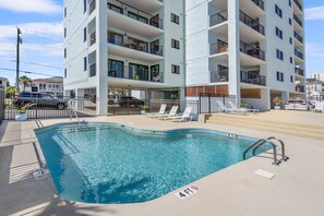 A swimming pool with a 4ft depth marker, surrounded by a deck with lounge chairs, and a multi-story building with balconies in the background. - Superb oceanfront condo w/pool, sundeck, private balcony near pier for fishing, walking, crabbing (North Myrtle Beach)