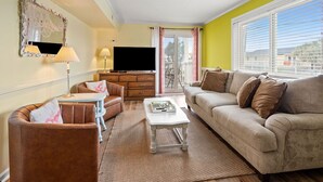 A living room with a sofa, armchair, coffee table, TV, and a balcony with a view. - Your Classic Oceanfront Retreat in North Myrtle Beach! (North Myrtle Beach)