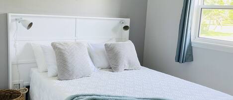A neatly arranged bedroom with a bed, a ceiling fan, a macrame wall hanging, and a window with curtains.