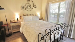 Un lit bien fait, avec un cadre en métal, deux tables de chevet avec des lampes, un élément de décoration murale et une fenêtre avec des rideaux.